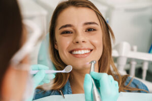 Smiling young woman receiving a dental checkup and cleaning from a dentist wearing gloves in a modern dental clinic.