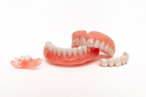 A set of dentures and dental prosthetics, including full upper and lower dentures and partial dental bridges, displayed on a white background.